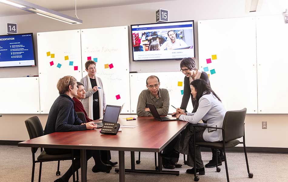 An image of Language Sciences members sitting at a table in front of a lit wall and a tv screen