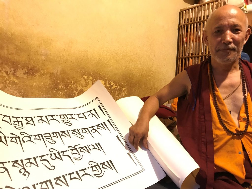 A picture of a Tibetan monk holding a large scroll upon which Tibetan characters are written.