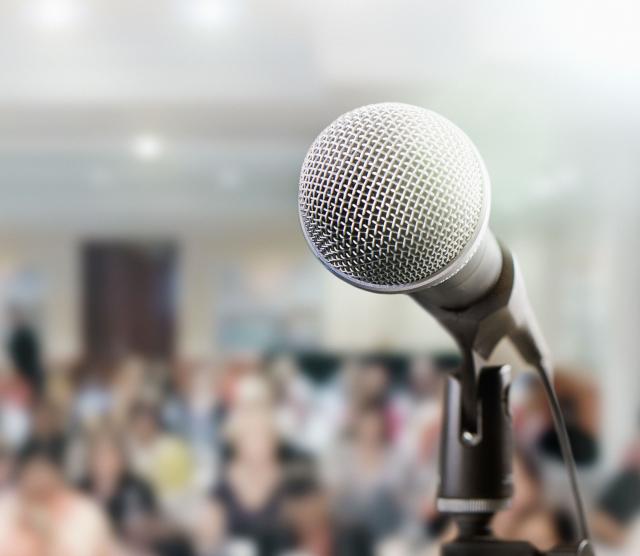 Image of a microphone in the foreground of a lecture hall