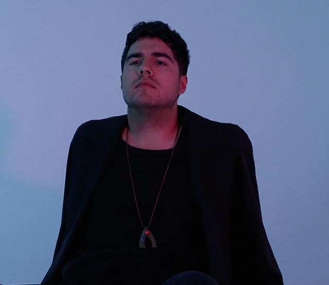 A picture of Jeremy Dutcher standing in front of a blue wall