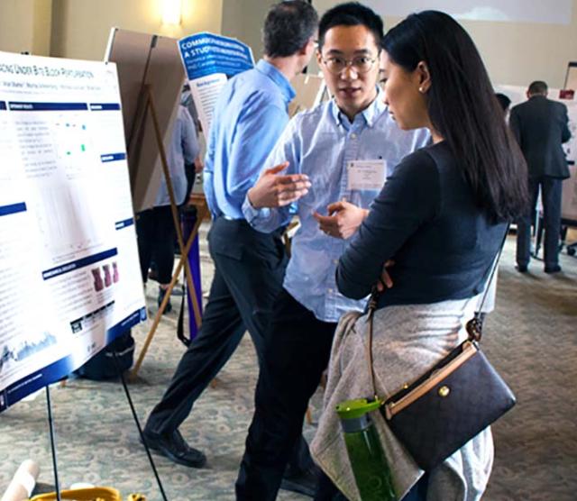 An image of Yadong explaining his poster to Rachel, with Bryan Gick in the background