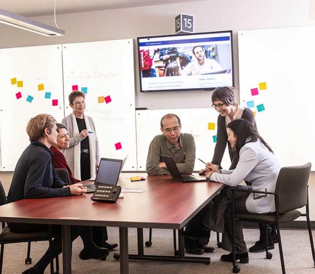 An image of Language Sciences members sitting at a table in front of a lit wall and a tv screen
