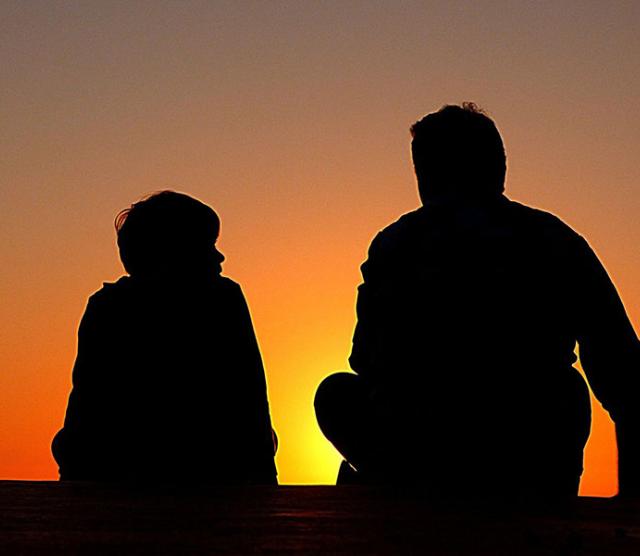 Silhouettes of an older man and child against the setting sun