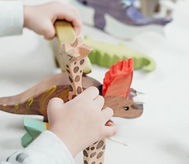 A close up of a child's hands playing with a wooden triceratops and a wooden giraffe