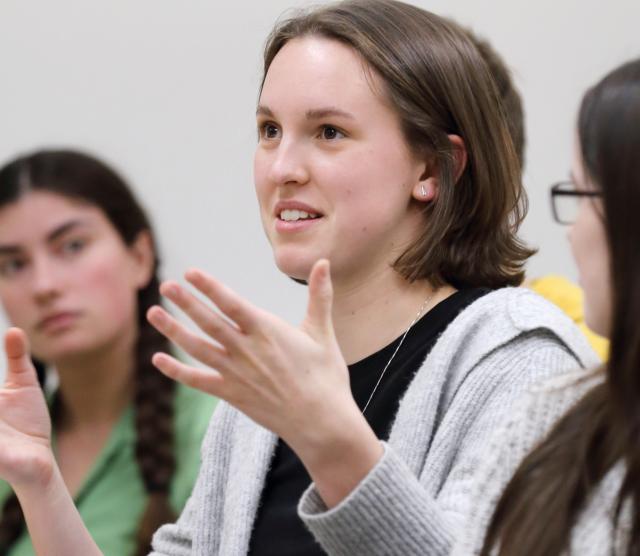 An image of Lauren speaking, gesturing with her hands, while classmates listen to her