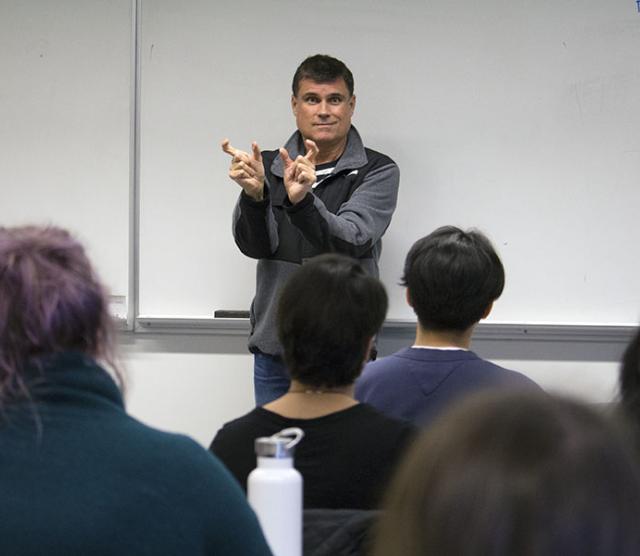 A photo of Nigel Howard standing in front of a class teaching ASL