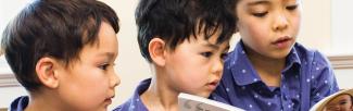 A photo of three children in blue shirts reading the ABCs for New Parents book