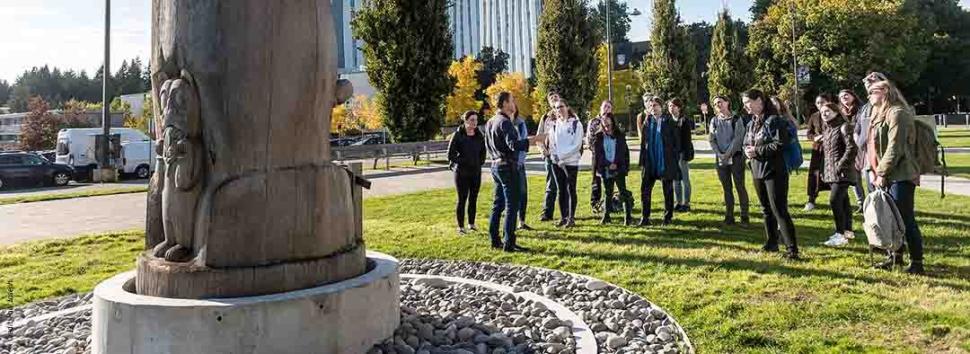 A picture of the Reconciliation Pole at UBC, in front of which Mark Turin is speaking to the Living Language class