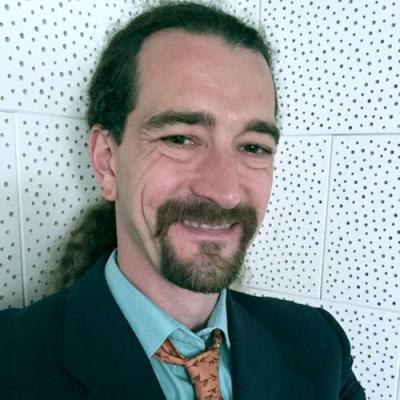 A picture of Professor Newman wearing a blue shirt, black jacket and orange tie.