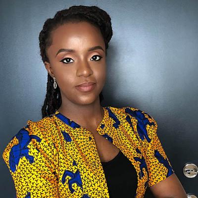 A headshot of Ifeoluwanimi Adebara wearing a yellow and blue shirt, standing in front of a dark door