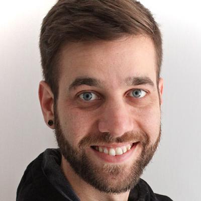 A headshot of Félix Desmeules-Trudel wearing a black hoodie and a black ear plug, smiling at the camera against a white background