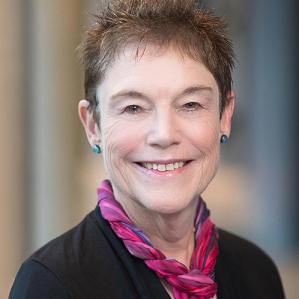 A headshot of Bonny Norton smiling, wearing a black sweater and pink scarf