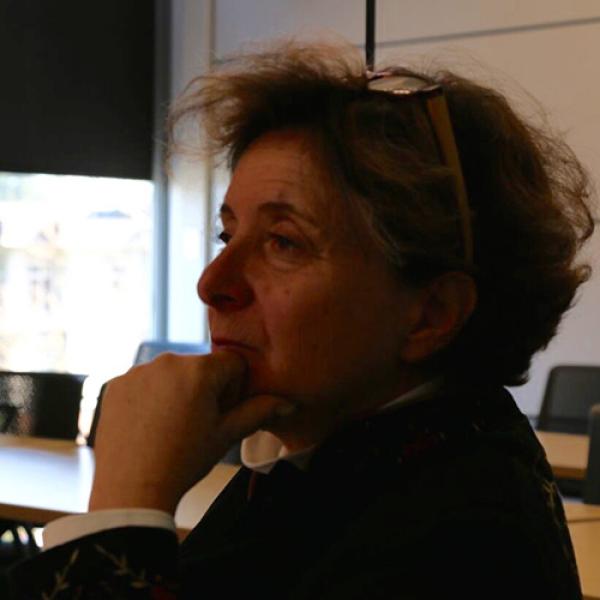 A headshot of Judy Illes facing to the left, resting her chin in her hand, and with glasses on her head